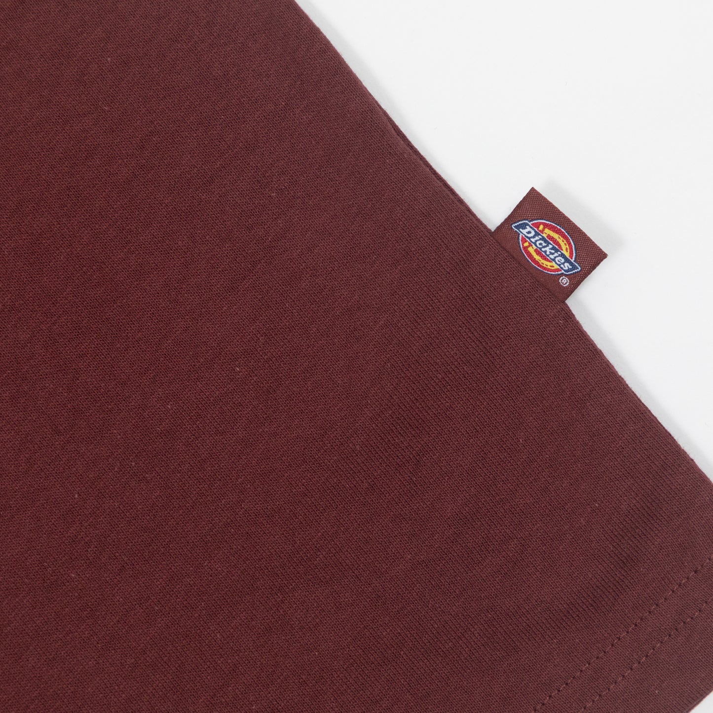 Close-up of a maroon shirt with a Dickies logo tag on a white background