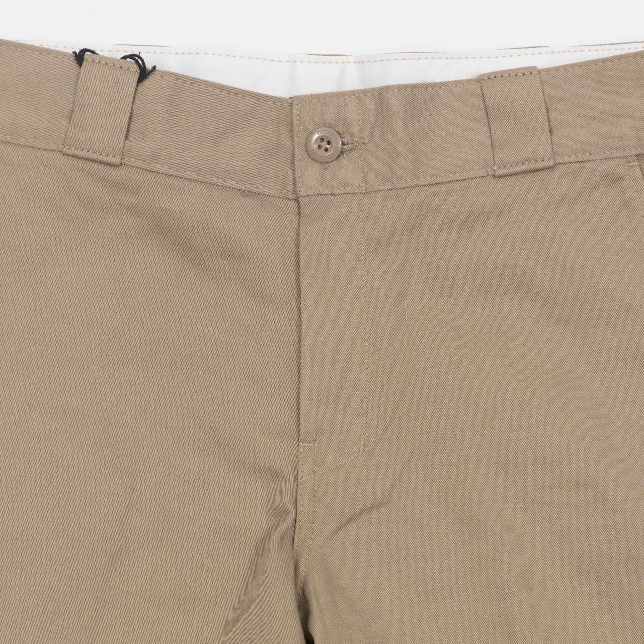 Close-up of beige dickies trousers with a button and zipper on a white background